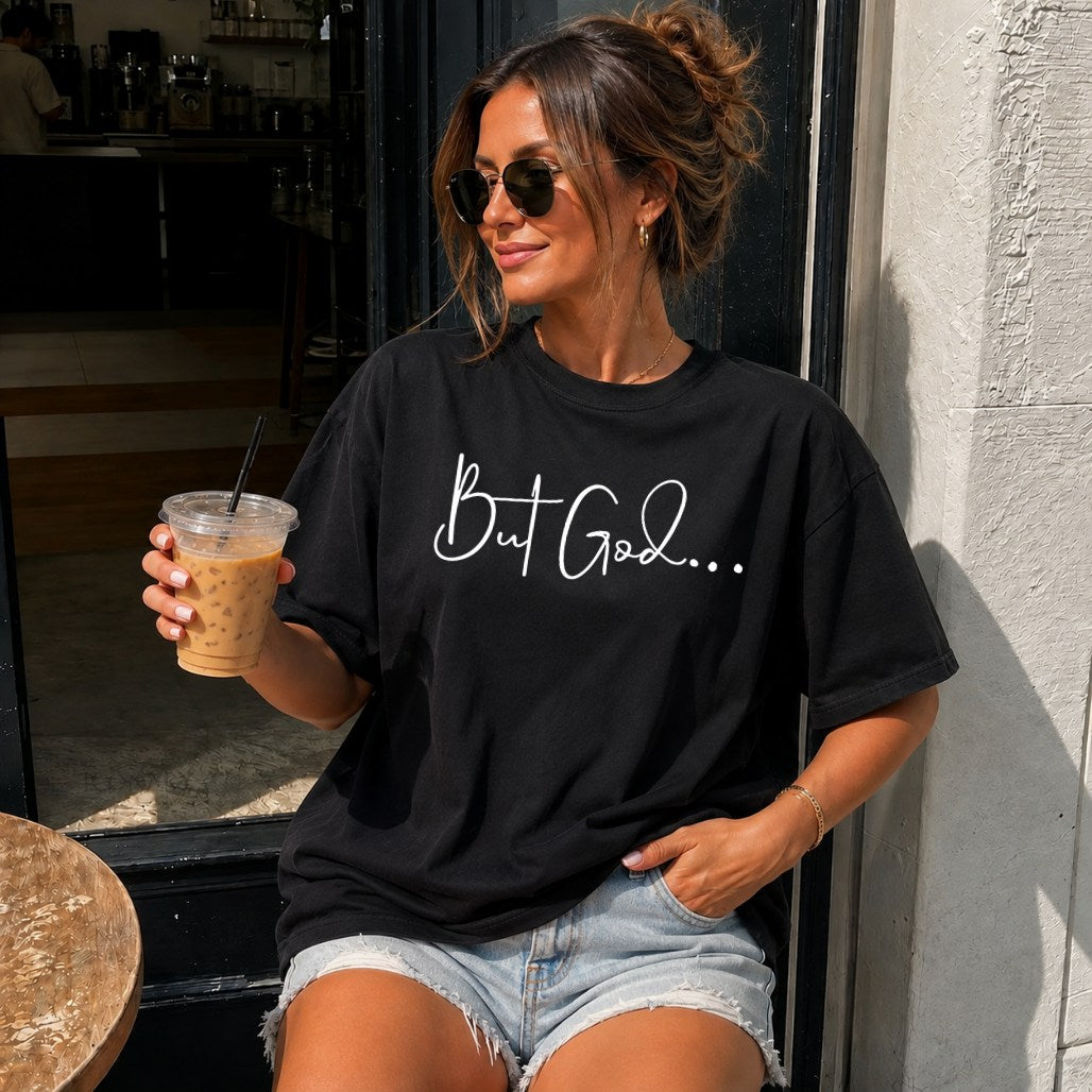Woman wearing a But God Christian faith t-shirt, holding an iced coffee outside a cafe